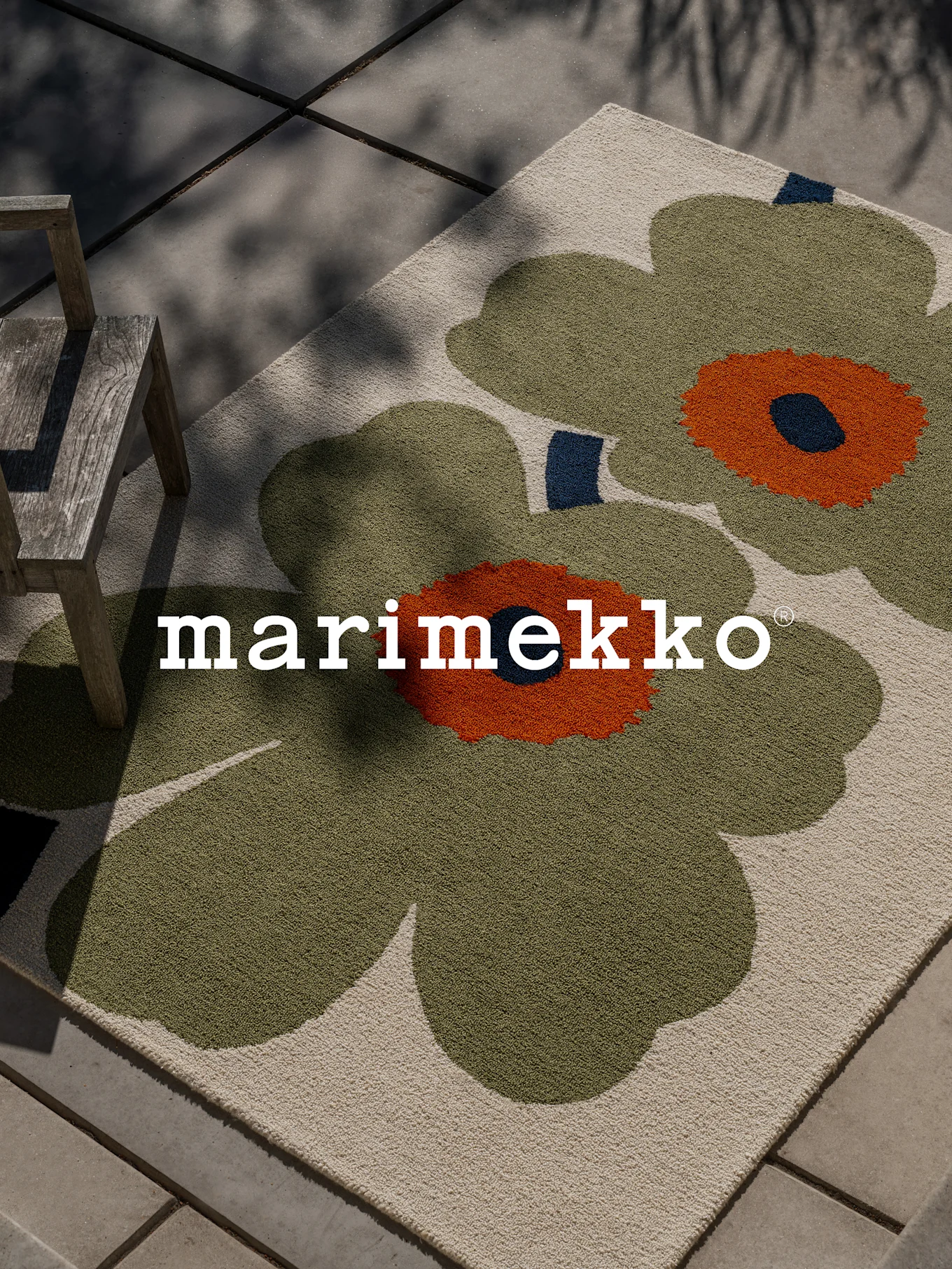 Marimekko vloerkleed met groot groen en oranje bloemenpatroon op een terras met houten stoel.
