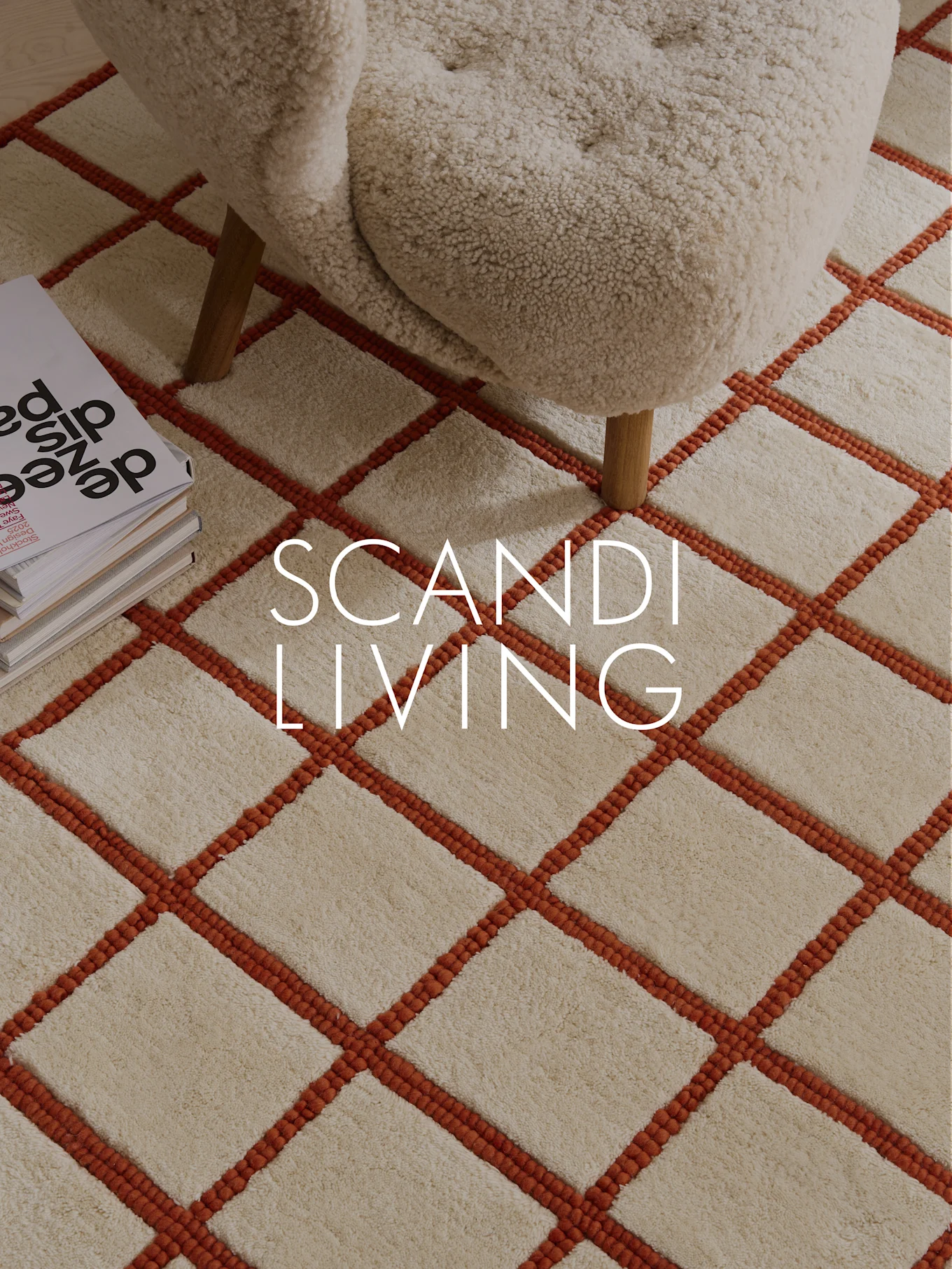 Crèmekleurig hoogpolig vloerkleed met oranje rasterpatroon, crèmekleurige fauteuil en boeken. Tekst: SCANDI LIVING.