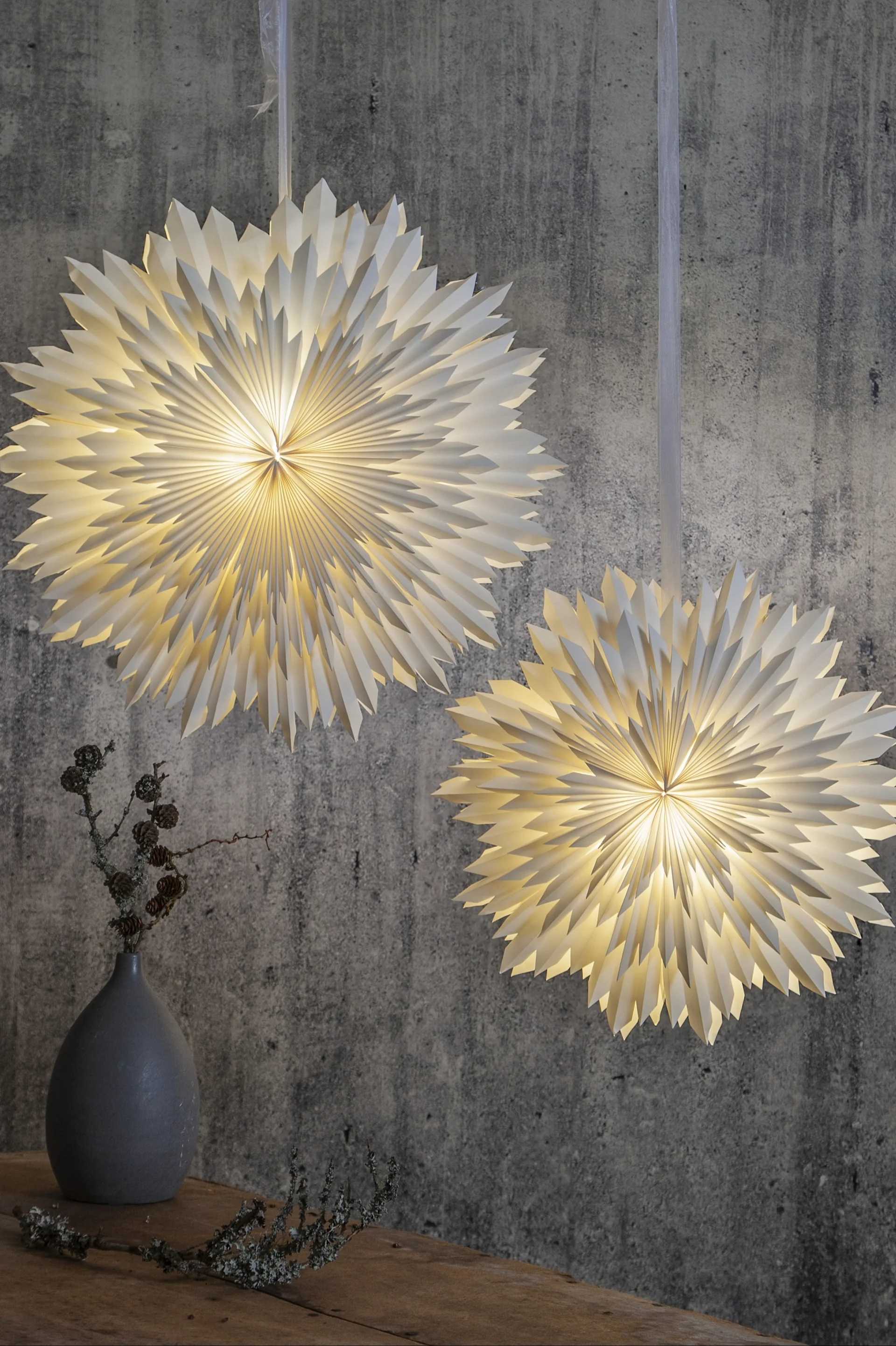 De kerstster Ice van Star Trading hangt in een duo tegen een grijze muur.